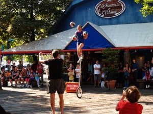 He's juggling while on a really tall unicycle.